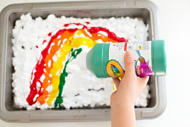 Pouring paint in a shallow pan filled with shaving cream to make rainbow shaving cream