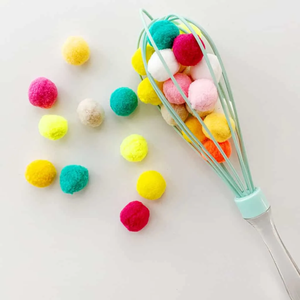 Pom poms and kitchen whisk activity to practice fine motor and sensory skills. 