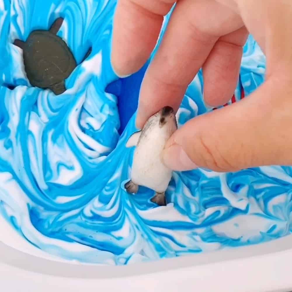 penguin toy in a frozen shaving cream sensory bin 