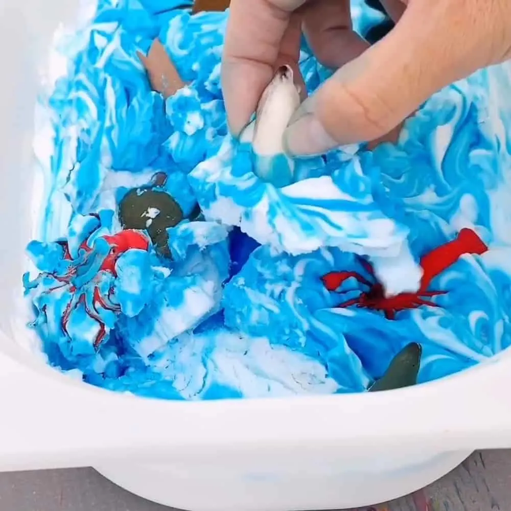 penguin toy in a frozen shaving cream sensory bin 