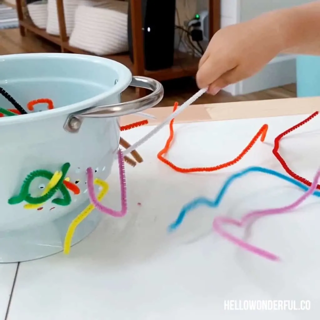 toddler grabbing pipe cleaners in colander to practice fine motor skills 