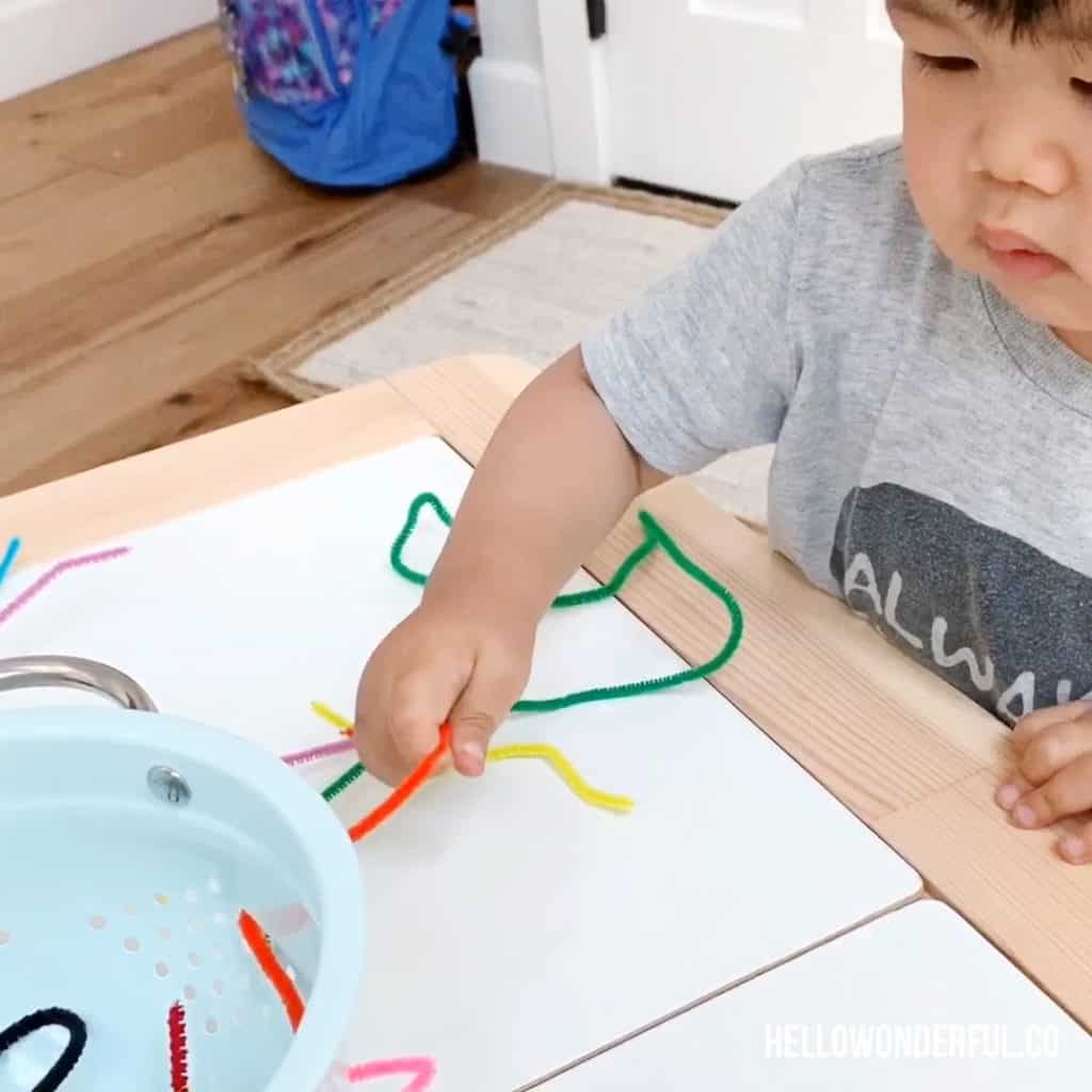 toddler grabbing pipe cleaners in colander for fine motor skills 