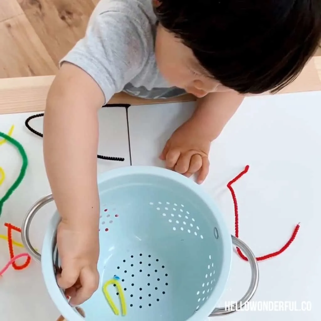 toddler grabbing pipe cleaners in colander for fine motor skills 