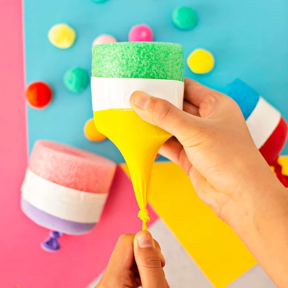 hand stretching yellow balloon to shoot out pom poms