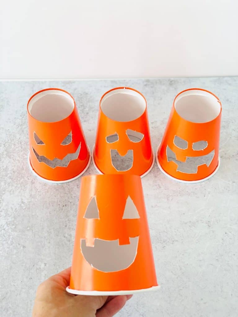 Orange paper cups cut into jack o' lantern faces for baking soda vinegar experiment.