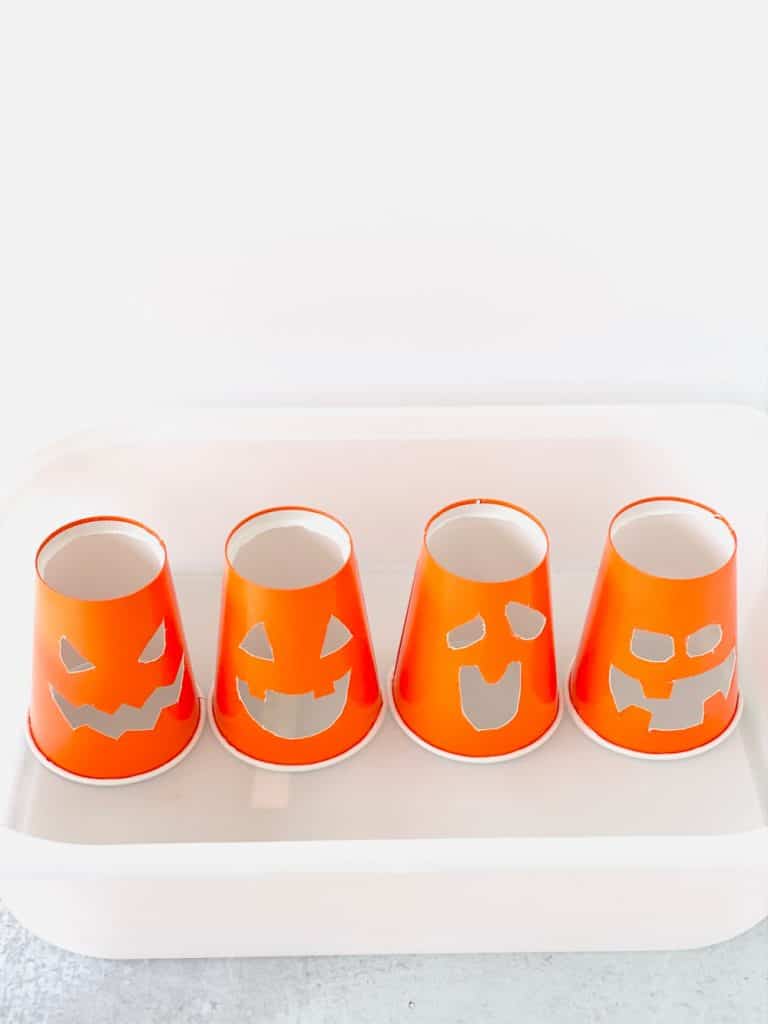 Orange paper cups cut into jack o' lantern faces for baking soda vinegar experiment.