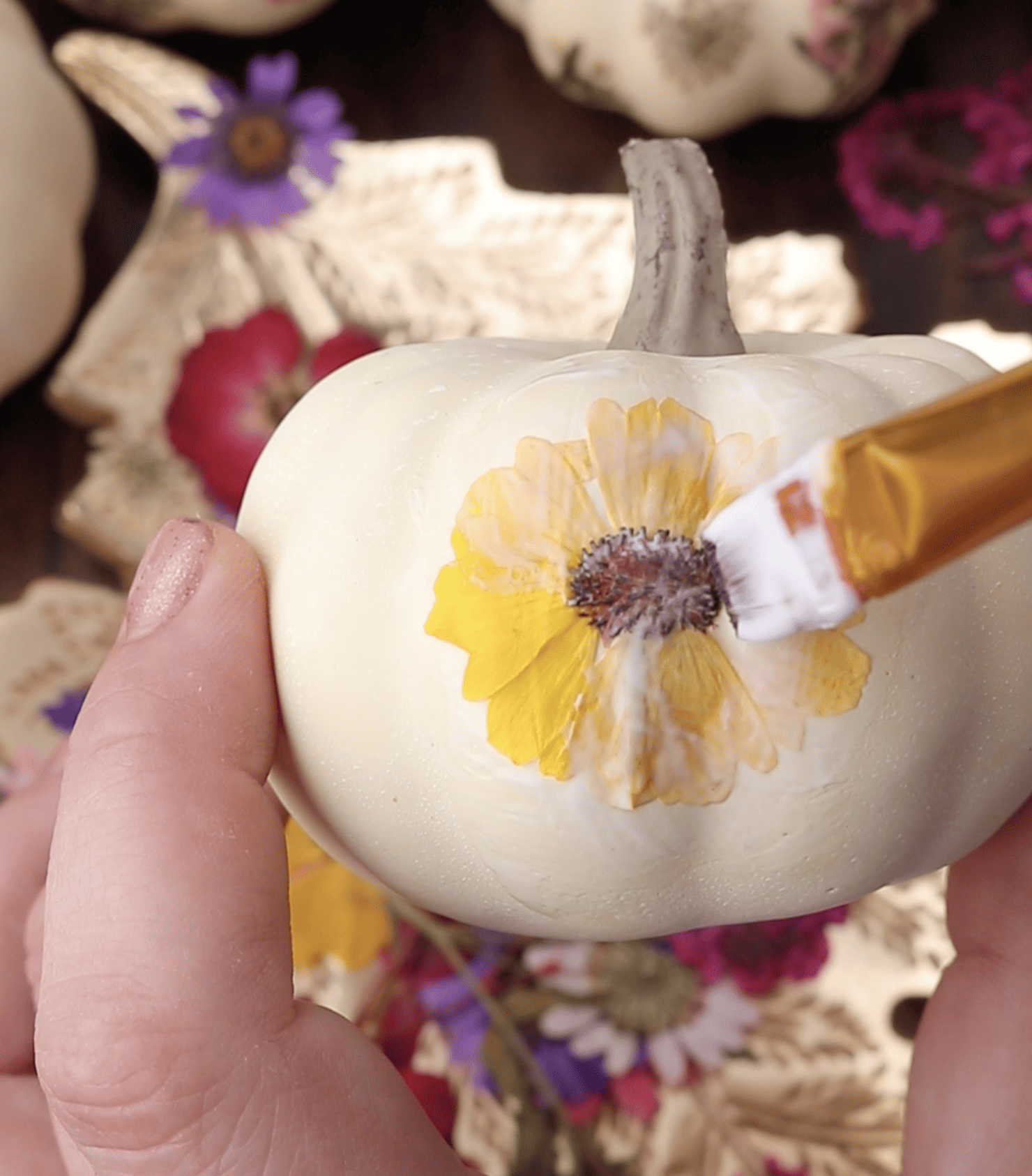 applying mod podge on a flower pressed onto a pumpkin